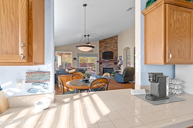 kitchen featuring light hardwood / wood-style flooring, tile countertops, decorative light fixtures, vaulted ceiling, and a fireplace