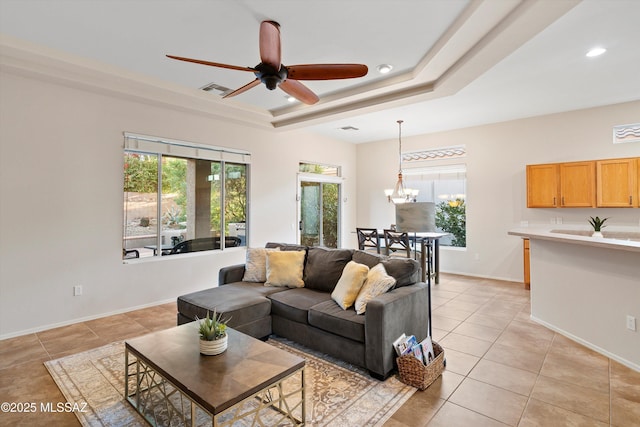 tiled living room with ceiling fan with notable chandelier and a raised ceiling