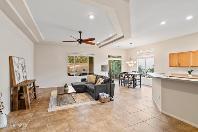 tiled living room with ceiling fan with notable chandelier and a raised ceiling