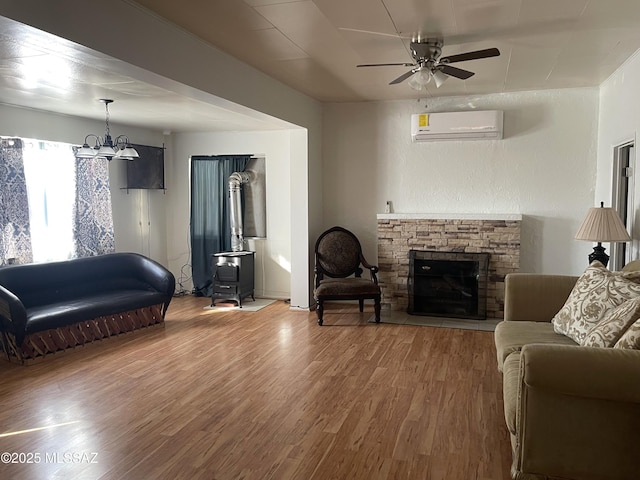 living room featuring a wall unit AC, a fireplace, wood-type flooring, and ceiling fan with notable chandelier