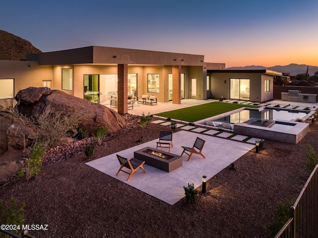 back house at dusk featuring a mountain view, a pool with hot tub, a patio, and an outdoor living space with a fire pit