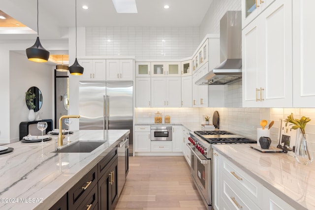 kitchen featuring pendant lighting, high quality appliances, white cabinets, sink, and wall chimney exhaust hood