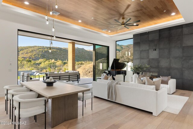 living room featuring light wood-type flooring, a raised ceiling, ceiling fan, wooden ceiling, and a mountain view