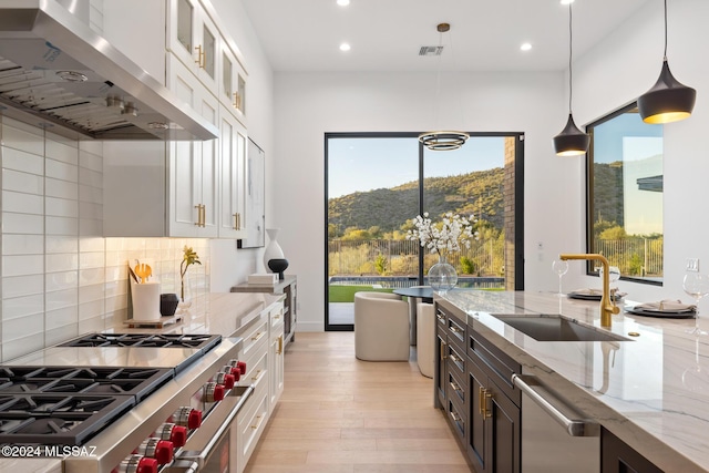 kitchen featuring sink, hanging light fixtures, light stone counters, ventilation hood, and white cabinets