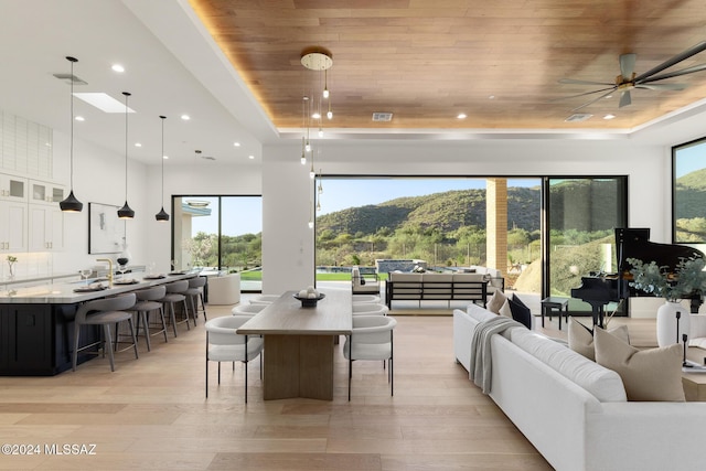 dining room featuring ceiling fan, a mountain view, a tray ceiling, wood ceiling, and light wood-type flooring