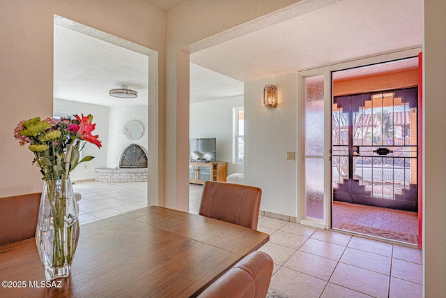 tiled dining room featuring a brick fireplace, a healthy amount of sunlight, and a textured ceiling