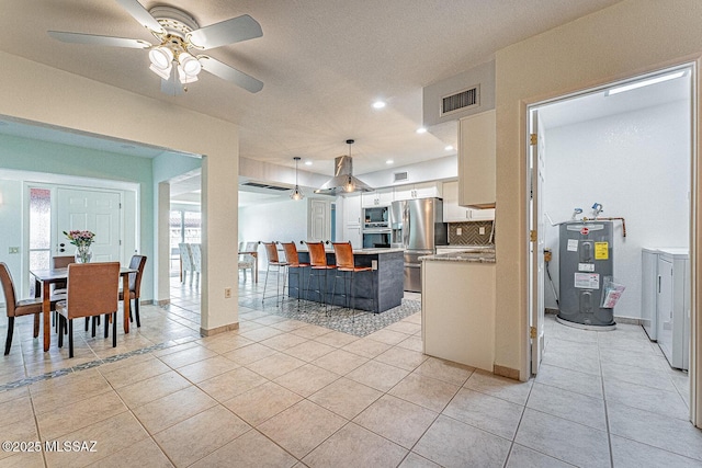 kitchen with decorative light fixtures, white cabinets, backsplash, stainless steel appliances, and electric water heater