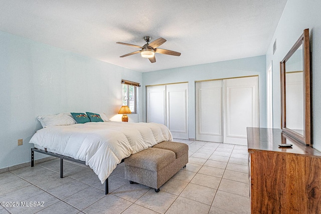 bedroom featuring ceiling fan, light tile patterned floors, a textured ceiling, and two closets