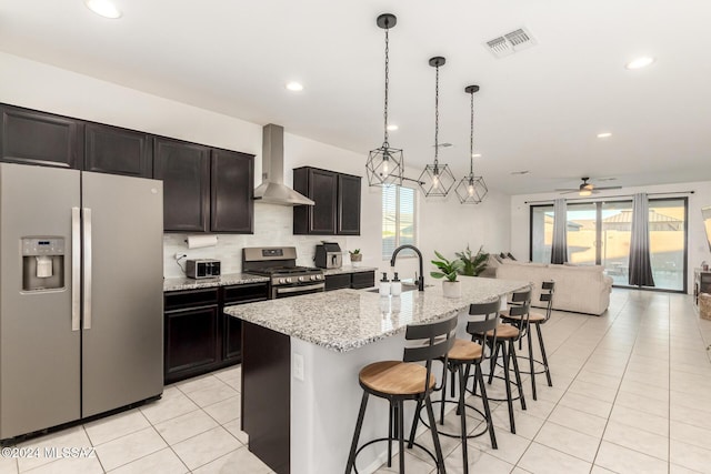 kitchen with a kitchen island with sink, wall chimney exhaust hood, a healthy amount of sunlight, and appliances with stainless steel finishes