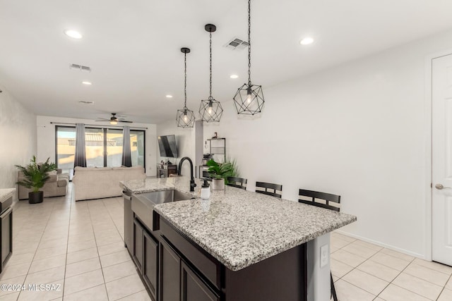 kitchen featuring a kitchen bar, ceiling fan, an island with sink, and decorative light fixtures