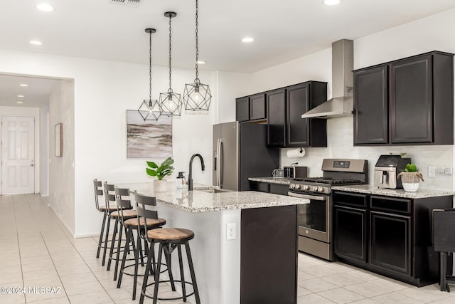 kitchen with pendant lighting, a kitchen island with sink, sink, wall chimney exhaust hood, and stainless steel appliances