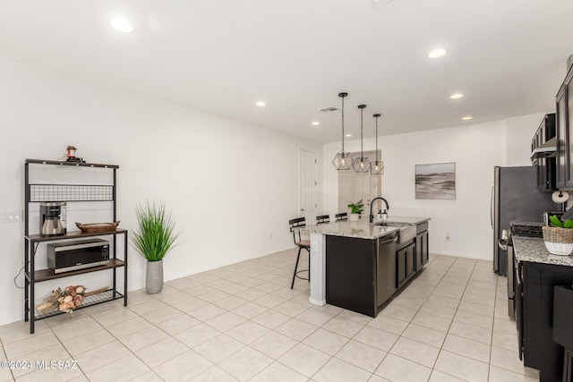 kitchen with a center island with sink, hanging light fixtures, light stone countertops, appliances with stainless steel finishes, and a breakfast bar area