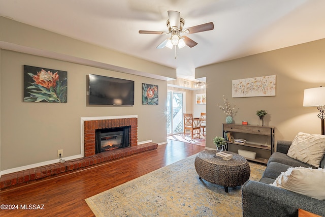 living room featuring ceiling fan, wood-type flooring, and a brick fireplace