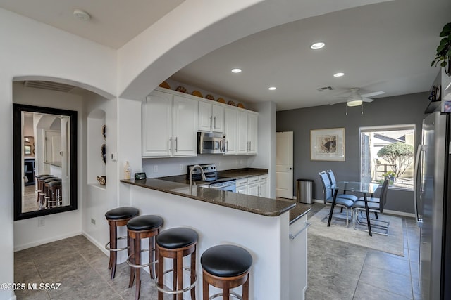 kitchen with white cabinets, a kitchen bar, ceiling fan, kitchen peninsula, and stainless steel appliances