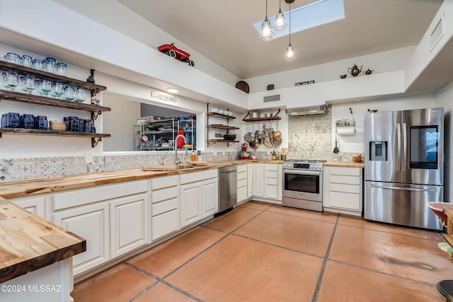 kitchen with decorative backsplash, appliances with stainless steel finishes, a sink, open shelves, and wooden counters