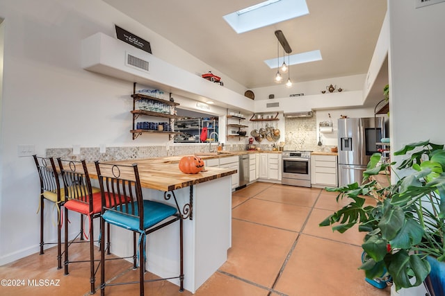 kitchen with a skylight, decorative backsplash, wood counters, stainless steel appliances, and open shelves