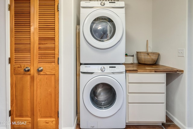 laundry room featuring stacked washer / dryer, cabinet space, and baseboards