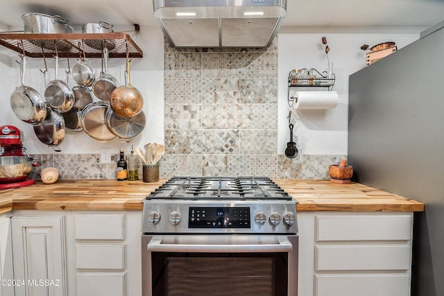 kitchen featuring stainless steel gas range oven, white cabinetry, wooden counters, decorative backsplash, and wall chimney exhaust hood