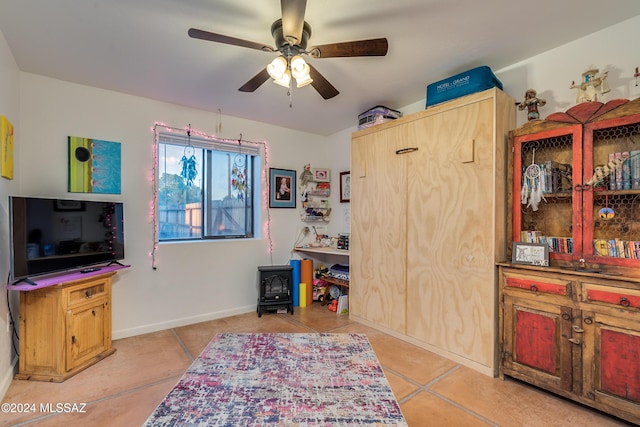 interior space featuring ceiling fan, a wood stove, and light tile patterned floors