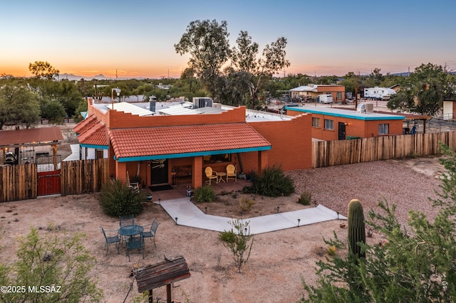 back of house at dusk with a tiled roof, a patio area, fence, and central air condition unit