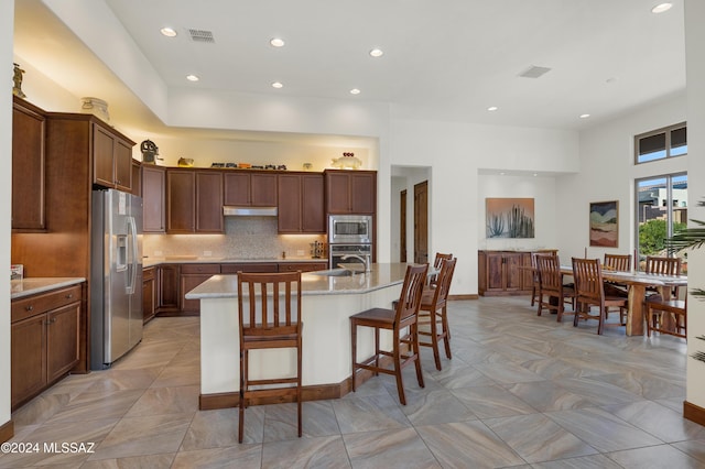 36513 S Cactus Ln, Tucson, AZ 85739 - kitchen with light stone counters, decorative backsplash, appliances with stainless steel finishes, under cabinet range hood, and a kitchen bar