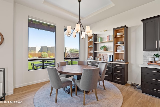 dining room featuring light wood-type flooring, baseboards, a raised ceiling, and a notable chandelier