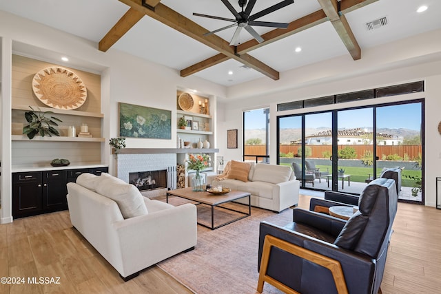 living room featuring beam ceiling, built in shelves, a fireplace, and light wood-type flooring