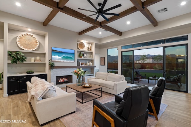 living area with coffered ceiling, visible vents, light wood-type flooring, a brick fireplace, and beamed ceiling