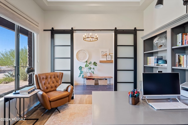 office area with a barn door, an inviting chandelier, wood finished floors, and baseboards