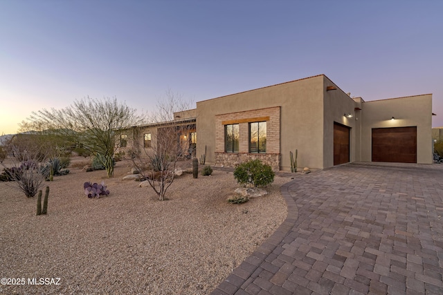 view of front facade featuring stone siding, decorative driveway, an attached garage, and stucco siding