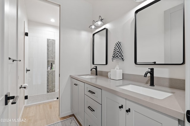 full bath featuring double vanity, a shower stall, a sink, and wood finished floors