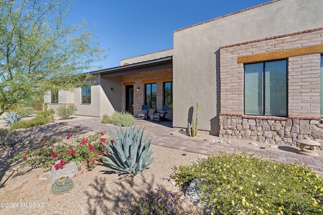 rear view of property with a patio, stone siding, and stucco siding