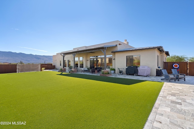 rear view of property featuring ceiling fan, a patio area, a mountain view, and a yard