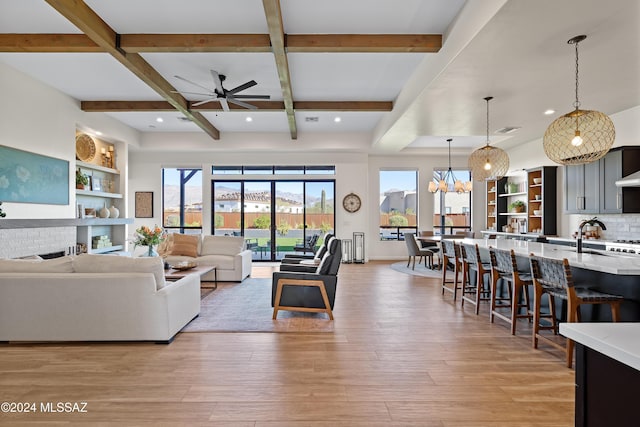 living room featuring ceiling fan with notable chandelier, coffered ceiling, a fireplace, light wood-type flooring, and beam ceiling