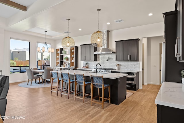 kitchen featuring visible vents, light wood-style floors, a sink, wall chimney range hood, and backsplash