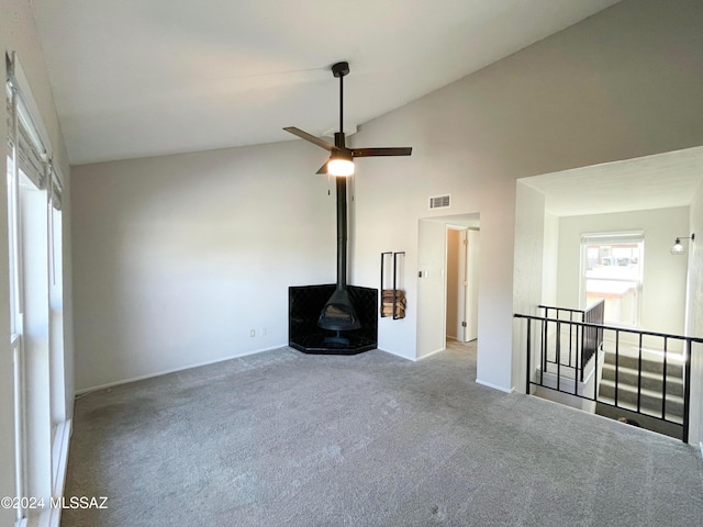 unfurnished living room with high vaulted ceiling, light colored carpet, a wood stove, and ceiling fan