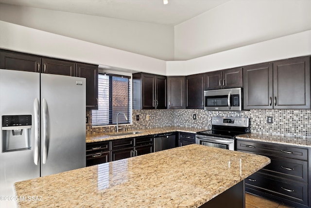 kitchen with light stone counters, stainless steel appliances, a sink, dark brown cabinets, and decorative backsplash