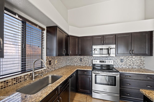 kitchen with light stone counters, appliances with stainless steel finishes, dark brown cabinets, and a sink