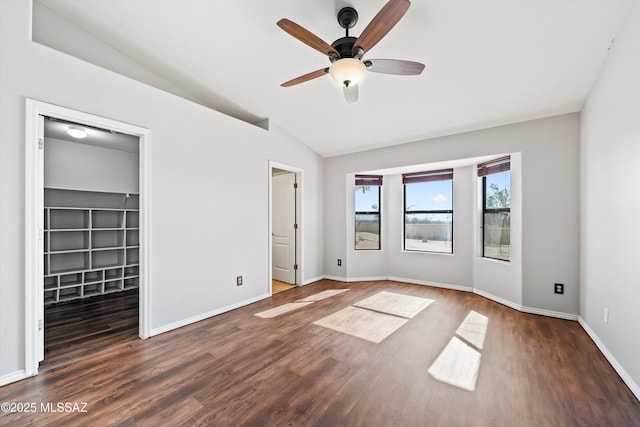 unfurnished bedroom featuring lofted ceiling, dark wood-style floors, baseboards, and a walk in closet