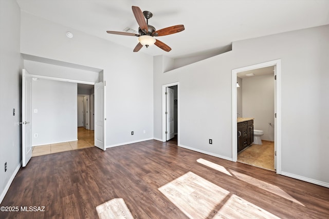 unfurnished bedroom featuring lofted ceiling, connected bathroom, baseboards, and wood finished floors