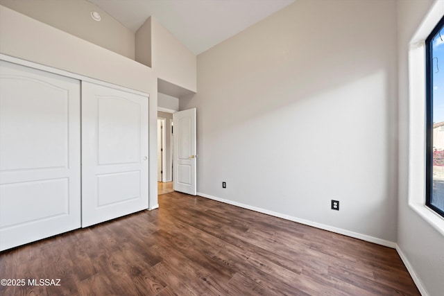 unfurnished bedroom with a closet, multiple windows, dark wood finished floors, and baseboards