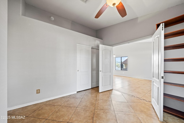 unfurnished bedroom featuring multiple closets, light tile patterned flooring, baseboards, and a ceiling fan