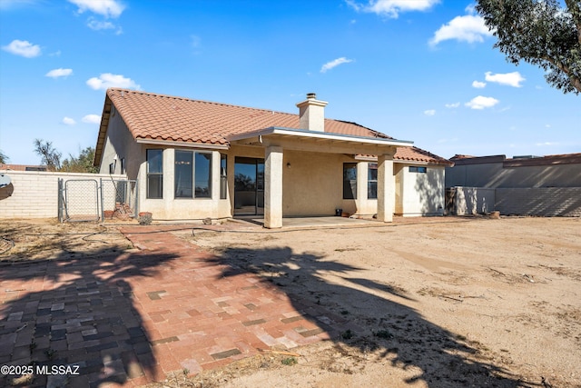 back of property featuring a patio, fence, a tile roof, stucco siding, and a chimney