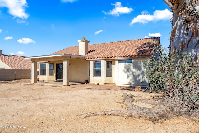 rear view of house with a patio, a tile roof, a chimney, fence, and stucco siding