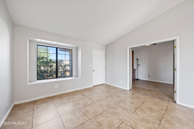 empty room with vaulted ceiling, light tile patterned flooring, and baseboards