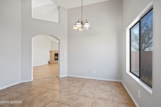 empty room featuring light tile patterned floors, a fireplace, a notable chandelier, and baseboards