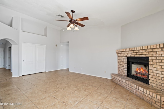 unfurnished living room with arched walkways, a fireplace, light tile patterned floors, visible vents, and a ceiling fan