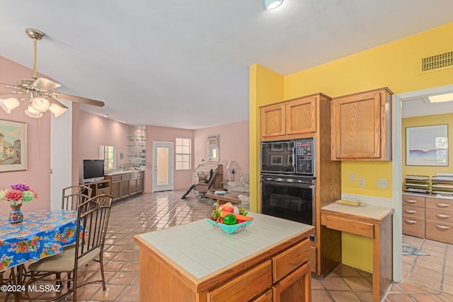 kitchen featuring tile countertops, light tile patterned flooring, black appliances, ceiling fan, and a kitchen island