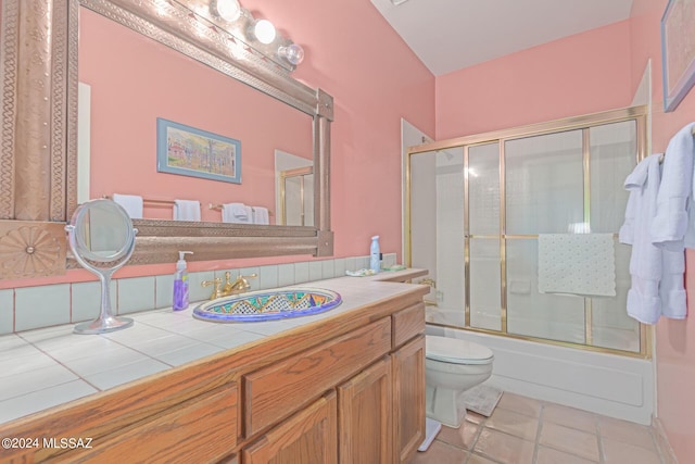 full bathroom with combined bath / shower with glass door, vanity, tile patterned flooring, and toilet