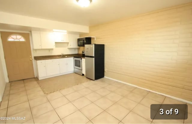 kitchen with sink, stainless steel appliances, white cabinets, brick wall, and light tile patterned flooring